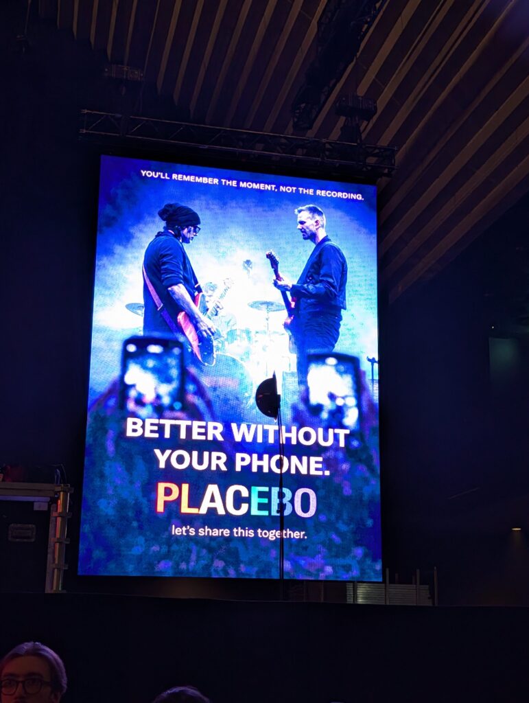 Storskärm före Placebos konsert med texten Better without your phone – let's share this together